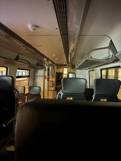 Der unbeleuchtete Innenraum eines bwegt Regionalzugs. Von außen vom Bahnsteig fällt Licht herein. Die Sitze sind leer.