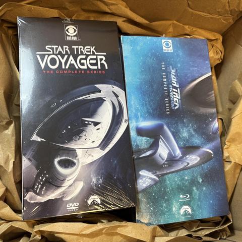 Jeweils die komplette Sammlung Stae Trek Voyager und TNG auf DVD und BluRay noch verpackt in einen Karton mit geöffnetem Deckel.