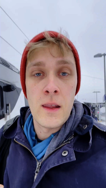 Ein Video in Selfie Perspektive, dass mich in Winterkjacke und Mütze von den Schultern aufwärts zeigt. Im Hintergrund ist ein Regionalzug und verschneiter Bahnsteig zu sehen.