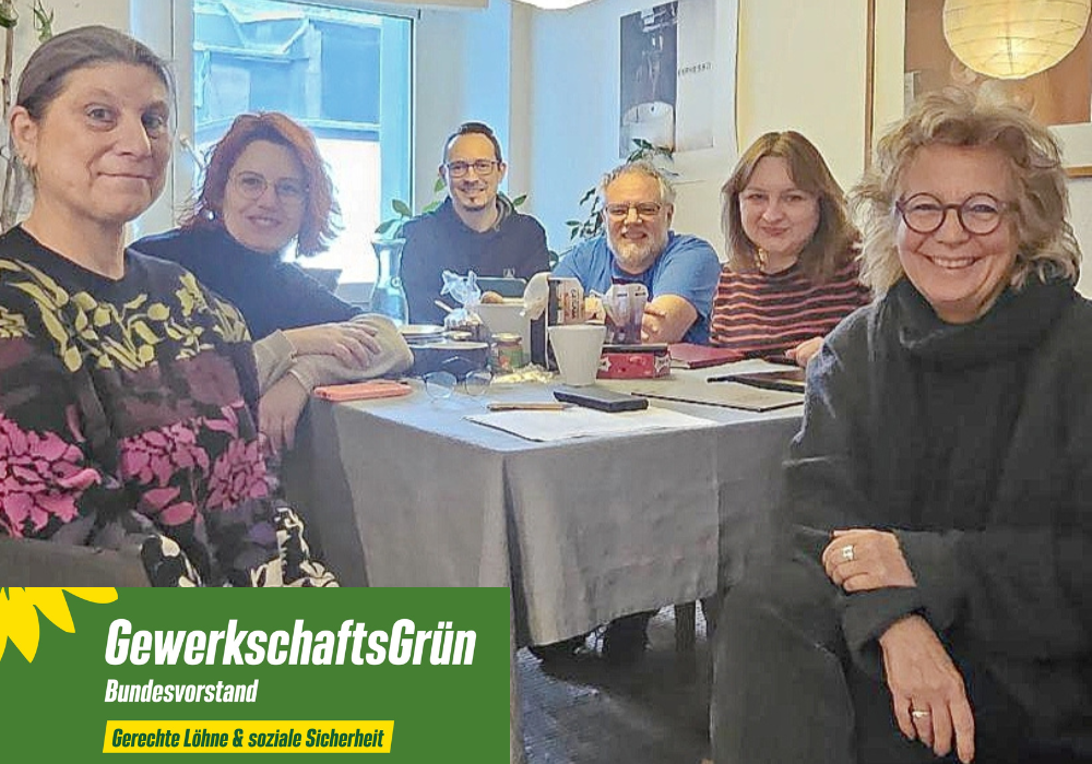 Gruppenfoto des Bundesvorstands von GewerkschaftsGrün in einem Innenraum: Sechs Personen sitzen an einem Tisch mit Laptops, Tassen und Unterlagen. Zu sehen sind (von links nach rechts) Yvonne Marchewitz, Klaudia Hanisch, Bernd Meffert und Dennis Kurzweil (Beisitzer:innen) sowie ganz links Sarah Gonschorek und ganz rechts Beate Müller-Gemmeke, die beiden Sprecherinnen von GewerkschaftsGrün. Die Gruppe blickt in die Kamera, die Atmosphäre wirkt konzentriert und kollegial.