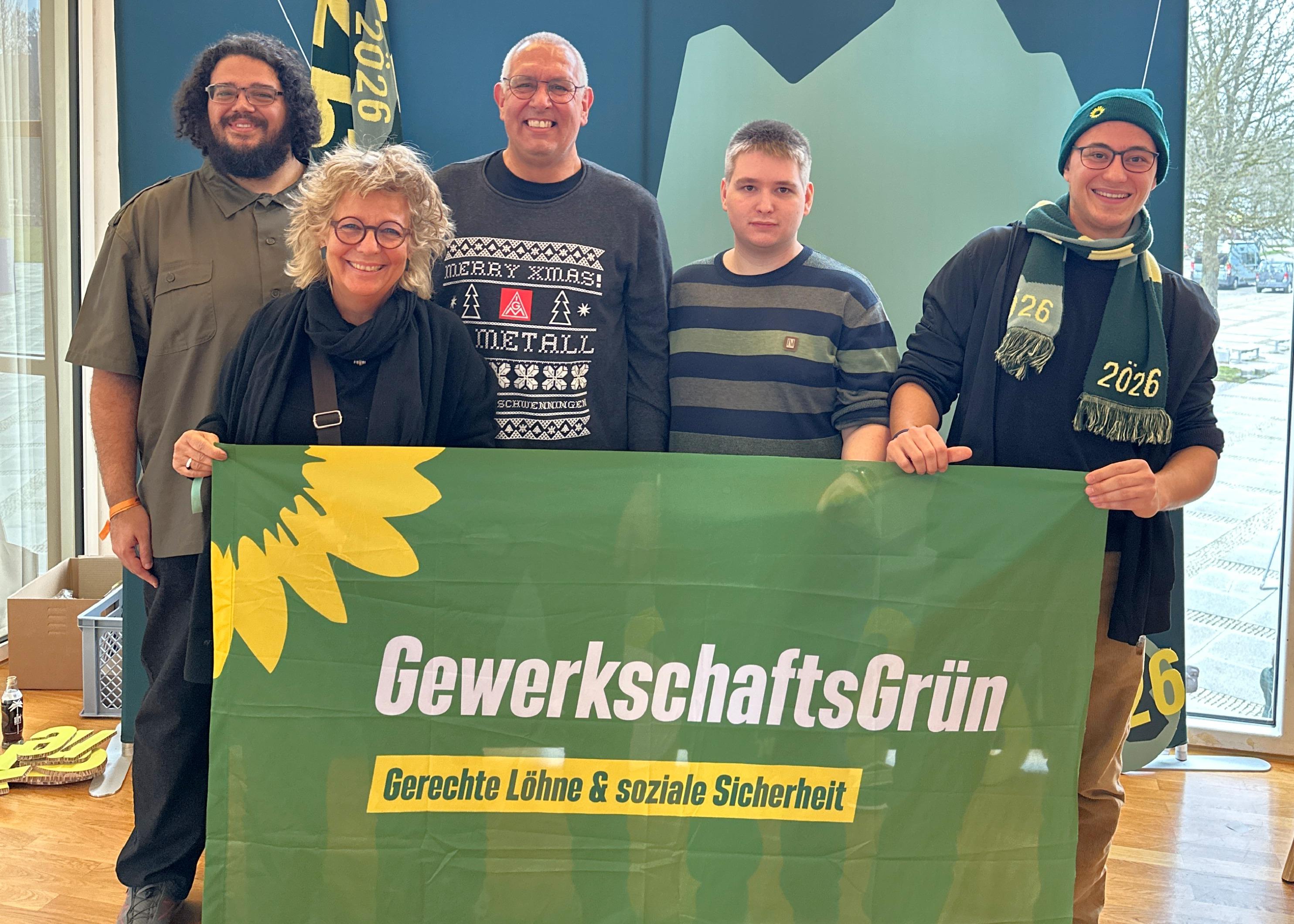 Fünf Personen stehen bei der Landesdelegiertenkonferenz (LDK) der Grünen in Ludwigsburg in einem hellen Saal und halten ein grünes Banner mit der Aufschrift „GewerkschaftsGrün – Gerechte Löhne & soziale Sicherheit“. In der Mitte steht Beate Müller-Gemmeke. Im Hintergrund sind große Fenster und Materialien zur LDK zu sehen.