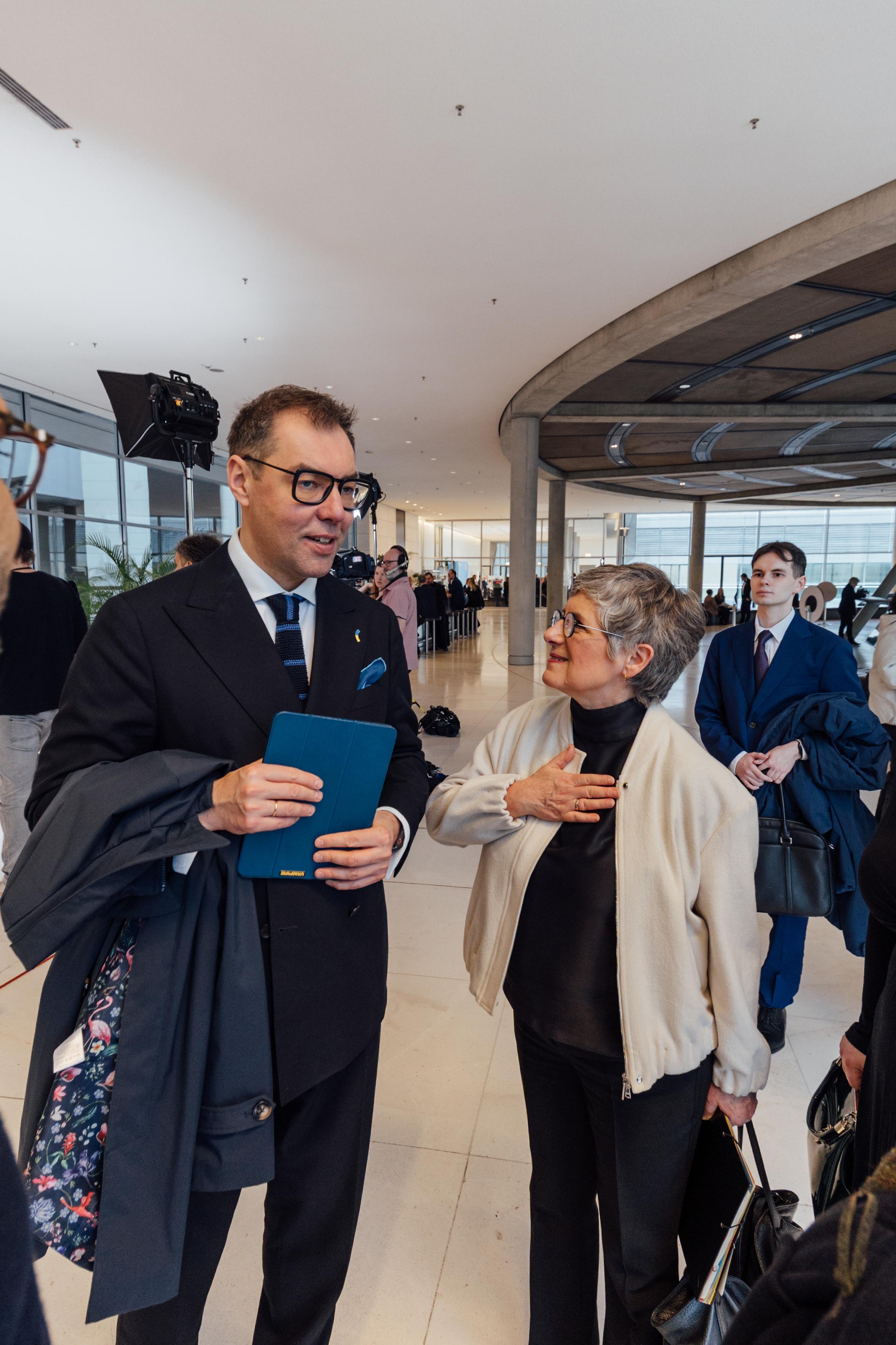 Der ukrainische Botschafter Oleksii Makeiev steht auf der Fraktionsebene des Bundestages. Neben ihm steht Britta Haßelmann. Sie schaut den Botschafter an und fasst sich ans Herz. Um sie herum stehen Menschen.