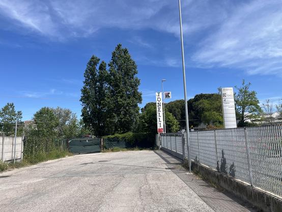 A dead end road with industry to the right. Trees beyond are in Italy 